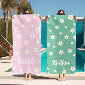 May include: Two pink and green beach towels with white daisy patterns. The towels have the names "Debbie" and "Kaitlyn" printed on them.