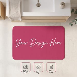 May include: A rectangular dark pink bath mat featuring the white cursive text Your Design Here centered on the surface. Below the mat are three square icons with labels: a camera icon labeled Photo, a geometric logo icon, and a document icon labeled Text.
