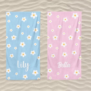 May include: Two beach towels with a daisy pattern. One towel is light blue with the name "Lily" printed on it. The other towel is pink with the name "Bella" printed on it.