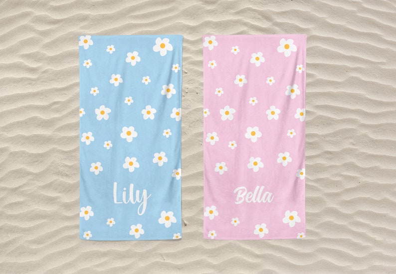 May include: Two beach towels with a daisy pattern. One towel is light blue with the name "Lily" printed on it. The other towel is pink with the name "Bella" printed on it.
