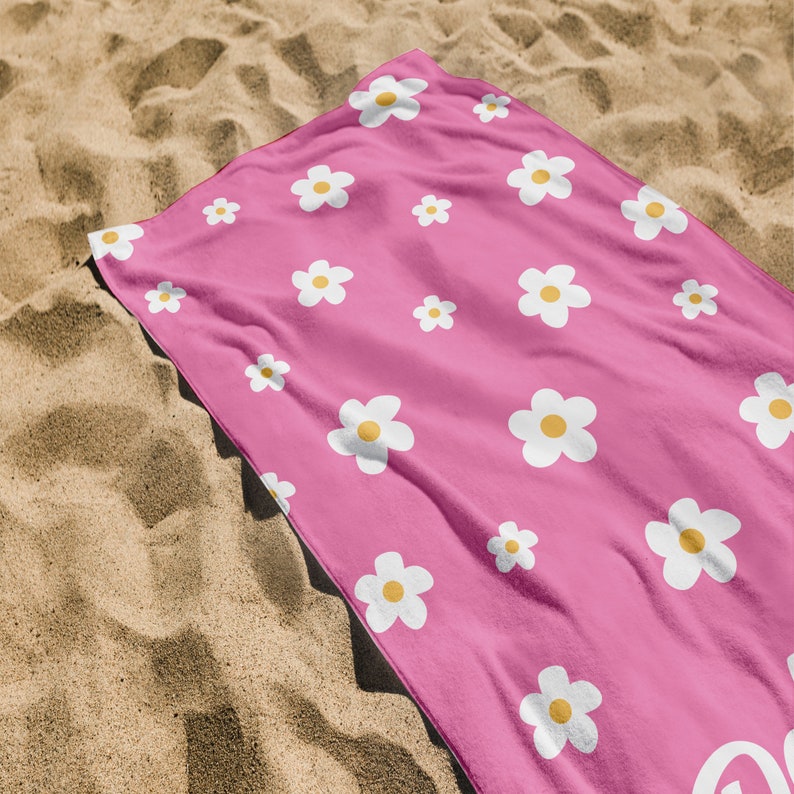 May include: Pink beach towel with a white daisy pattern. The daisies have yellow centers.
