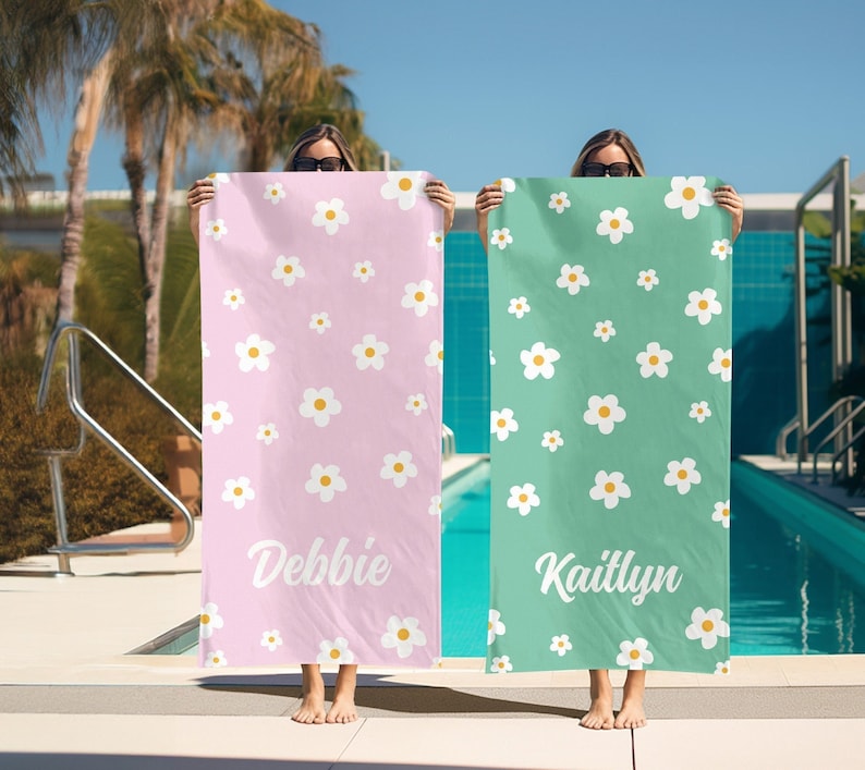 May include: Two pink and green beach towels with white daisy patterns. The towels have the names "Debbie" and "Kaitlyn" printed on them.