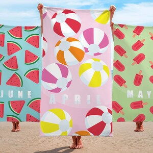 May include: Three beach towels with different designs. The first towel is blue with watermelon slices and the word "JUNE" printed on it. The second towel is pink with colorful beach balls and the word "APRIL" printed on it. The third towel is green with red popsicles and the word "MAY" printed on it.