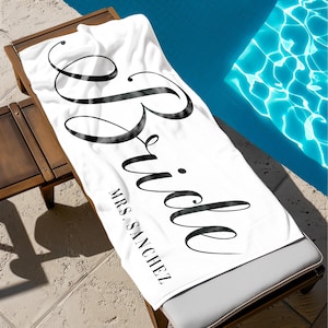 May include: White beach towel with the word "Bride" in black cursive lettering and the text "MRS. SANCHEZ" below.