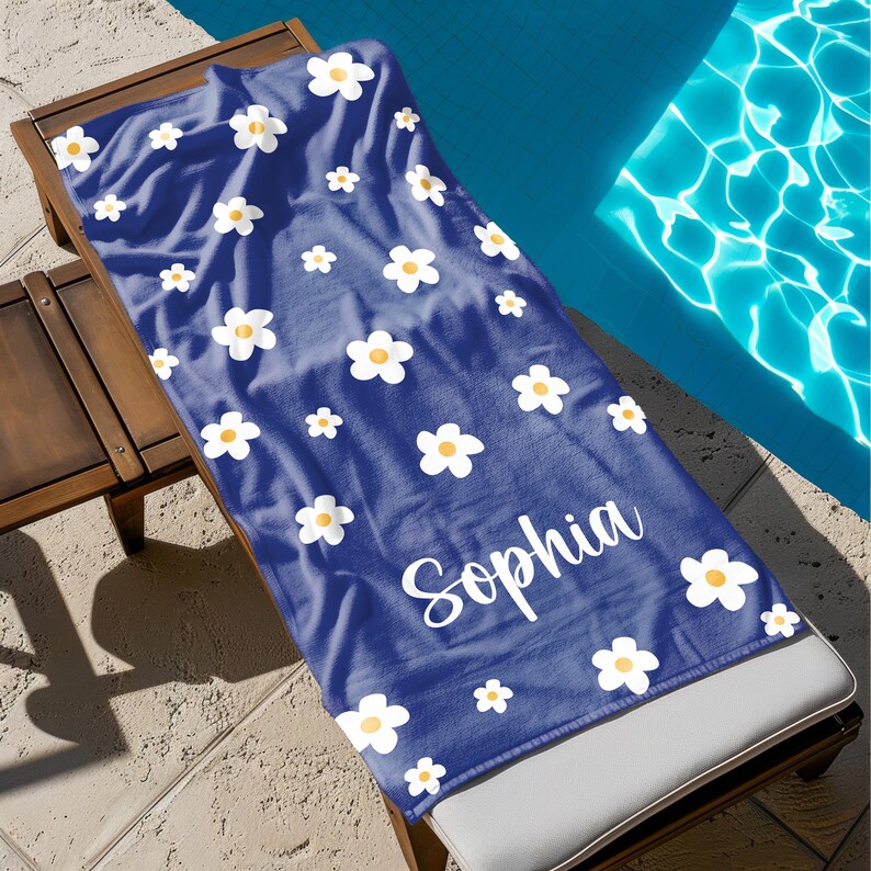 May include: A blue beach towel with a white daisy pattern and the name "Sophia" printed in white.