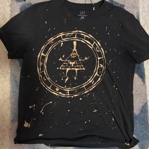 May include: Black t-shirt with a bleach-splattered design featuring a yellow triangle with an eye inside, surrounded by a circle with symbols. The text "[G] GEORGE" is visible on the shirt.