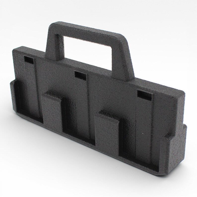 May include: A black plastic carrying case with a textured surface. The case has a handle and several rectangular cutouts and protrusions. The design suggests it is for organizing or transporting items.