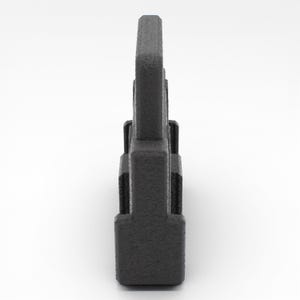 May include: A dark gray, textured, rectangular object with a vertical, tower-like design. The object has a series of stacked, rectangular sections, with a taller, central element. The surface has a slightly rough, matte finish.