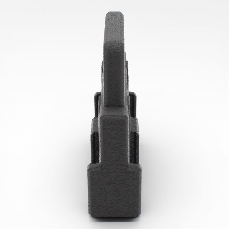 May include: A dark gray, textured, rectangular object with a vertical, tower-like design. The object has a series of stacked, rectangular sections, with a taller, central element. The surface has a slightly rough, matte finish.