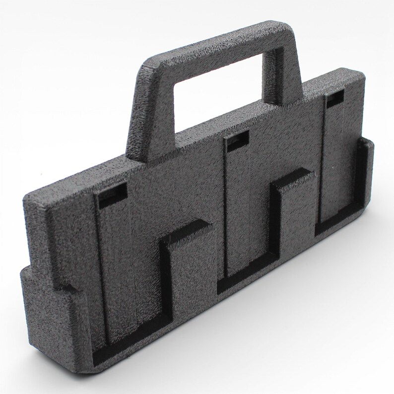 May include: A textured black plastic carrying case with a handle. The case has a rectangular shape with several recessed slots and a handle at the top for easy carrying. The surface has a slightly rough texture.