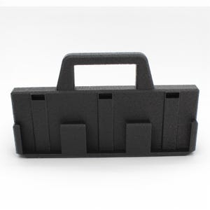 May include: A black plastic carrying case with a handle and multiple slots. The case has a textured surface and is designed to hold items. The handle is rectangular and is centered on the top of the case.