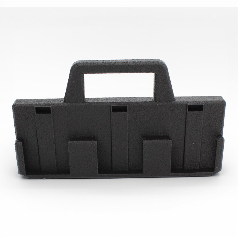 May include: A black plastic carrying case with a handle and multiple slots. The case has a textured surface and is designed to hold items. The handle is rectangular and is centered on the top of the case.