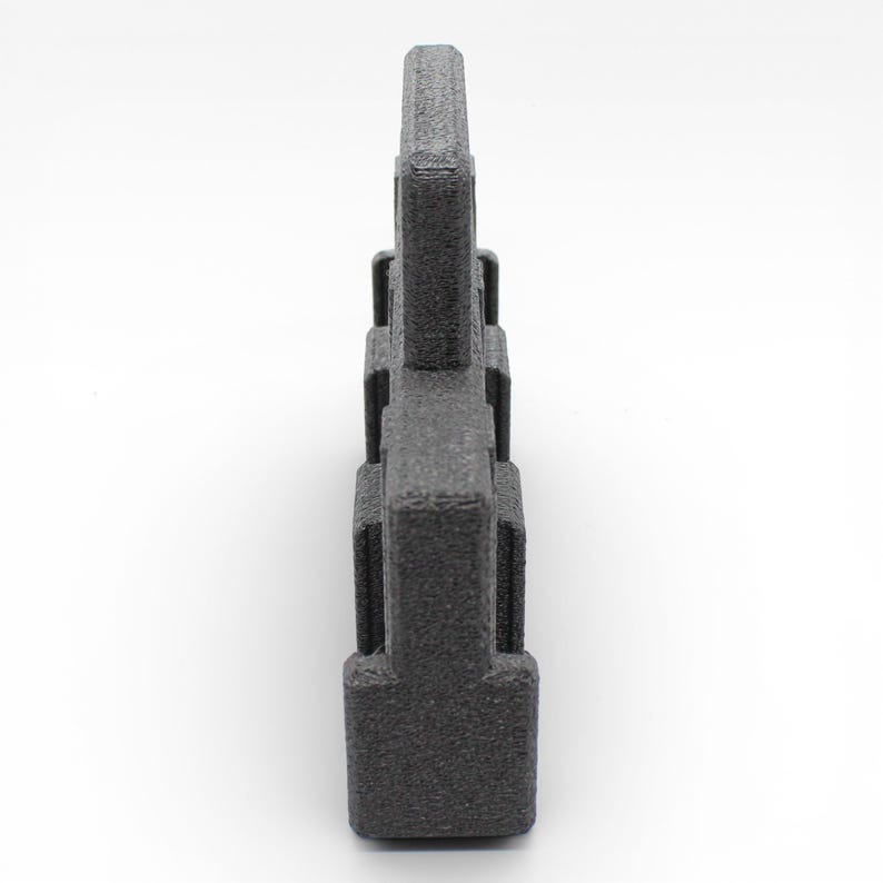 May include: A dark gray, textured, geometric object with a rectangular base and a series of stacked, rectangular blocks. The object has a rough, granular surface and is set against a white background.