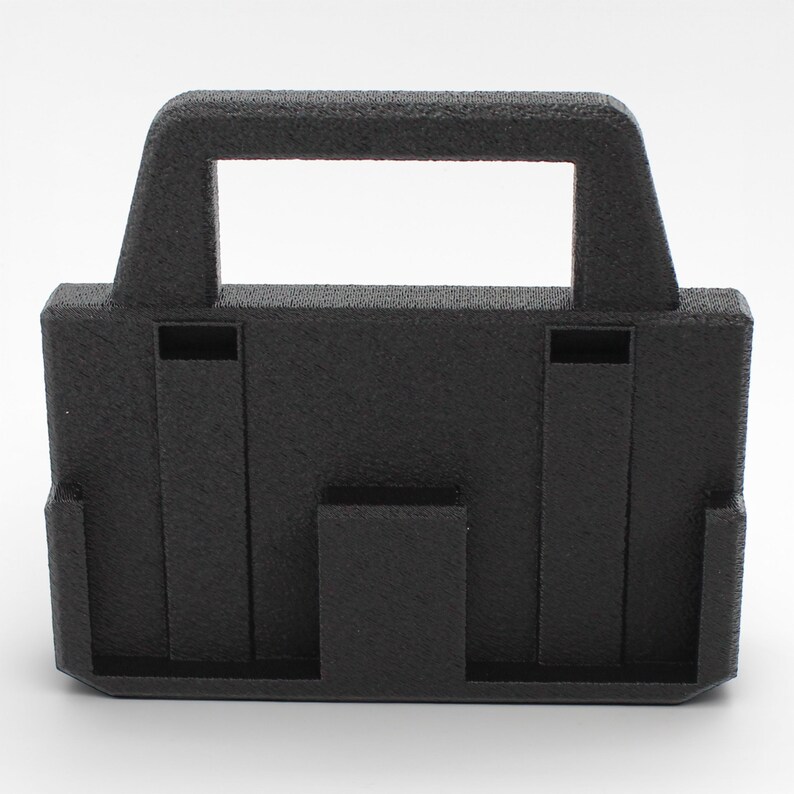 May include: A black, textured plastic object with a handle and rectangular cut-out. The object has a boxy shape with vertical and horizontal supports, and a textured surface. The design suggests a carrying case or holder.