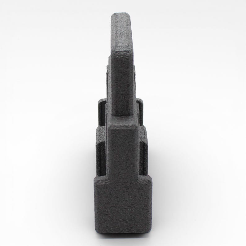 May include: A dark gray, textured, rectangular object with a handle-like top. The object has a series of rectangular protrusions along its sides. The item is set against a white background.