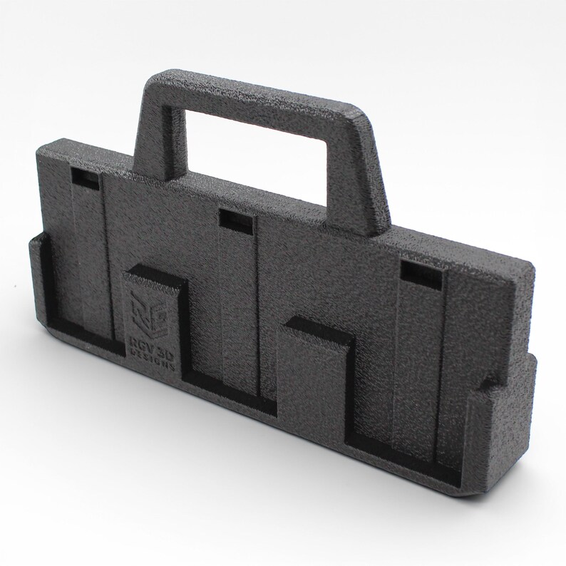 May include: A textured black 3D-printed carrying case with a handle. The case has a rectangular shape with several cut-out sections and the text "RGV 3D DESIGNS" on the front. The case is designed for carrying items.