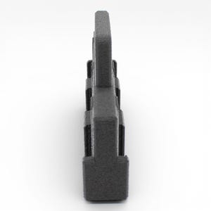 May include: A dark gray, textured, plastic object with a rectangular base and a series of vertical, rectangular protrusions. The object is viewed from the side against a white background. The overall shape resembles a stylized letter.