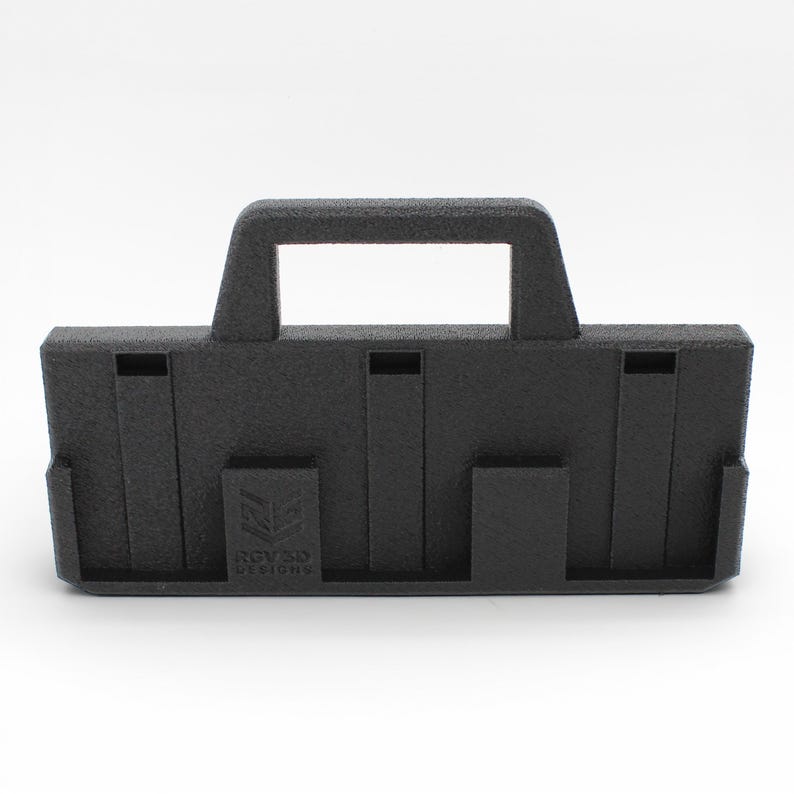 May include: A black, rectangular 3D-printed object with a handle and several slots. The object has a textured surface and the text "RGV 3D DESIGNS" is visible on the front. The design appears to be a carrying case or organizer.