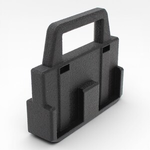 May include: A textured black plastic handle with a rectangular opening at the top. The handle has a rectangular base with two vertical slots and a smaller rectangular opening on the front.