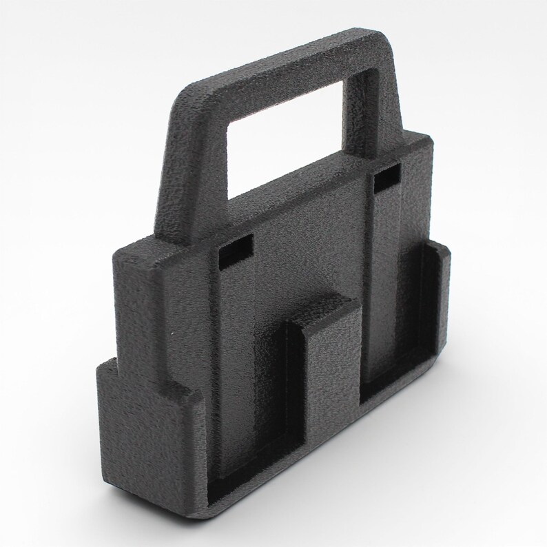 May include: A textured black plastic handle with a rectangular opening at the top. The handle has a rectangular base with two vertical slots and a smaller rectangular opening on the front.