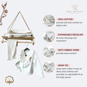 May include: White knitted baby sweater with a wrap tie, ruffled collar, and ribbed trims. The sweater is made of 100% cotton and has an expandable neckline for easy dressing. The text "100% COTTON" and "WRAP TIE" are visible in the image.