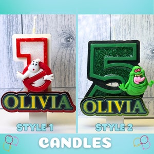 May include: Two Ghostbusters themed birthday candles, one with a red number 1 and the other with a green number 5. Both candles have a glitter finish and feature a Ghostbusters character. The candles are personalized with the name "Olivia" in yellow letters.