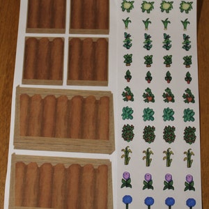 May include: Printable sheet of brown rectangular garden beds with a variety of green, red, and blue plant stickers. The stickers include flowers, vegetables, and bushes.