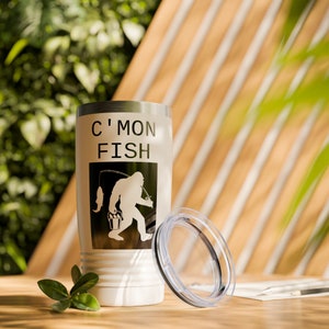 May include: White stainless steel travel mug with a black and white graphic of a Bigfoot holding a fishing rod and a bucket. The mug has the text "C'mon Fish" printed on it.