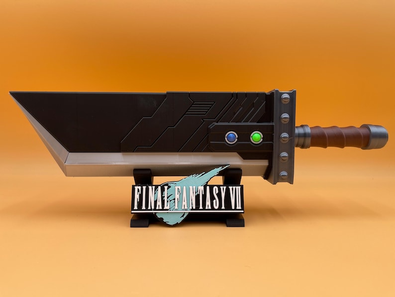 May include: A large, black and silver Buster Sword replica from Final Fantasy VII, with a brown handle and silver accents. The sword rests on a black stand with the Final Fantasy VII logo.