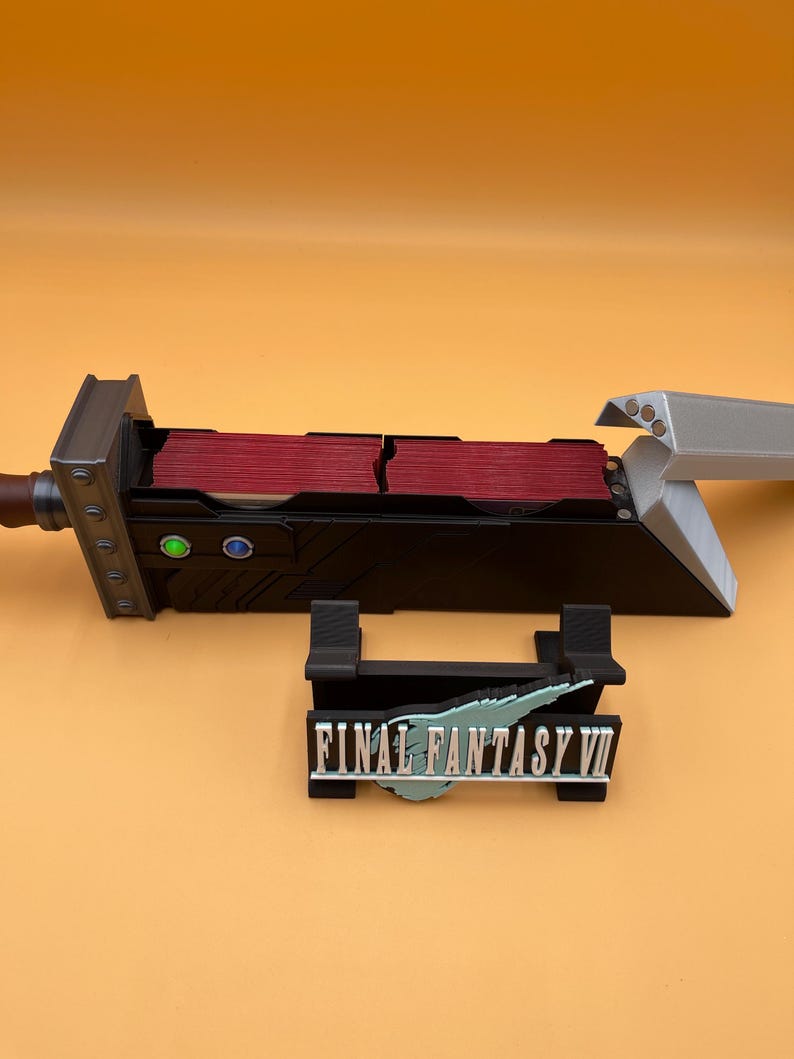 May include: A black and gray Final Fantasy VII themed card holder with a sword design. The holder has red card slots and a stand with the game's logo. The sword is silver and gray.