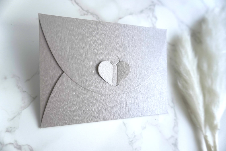 May include: A light gray envelope with a heart-shaped cutout. The cutout is filled with two overlapping hearts, one white and one gray.