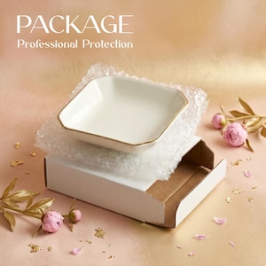 May include: A white square dish with gold trim rests on bubble wrap inside a white cardboard box. The image includes text that reads "PACKAGE Professional Protection". Pink flowers and gold leaf accents are scattered around the box.