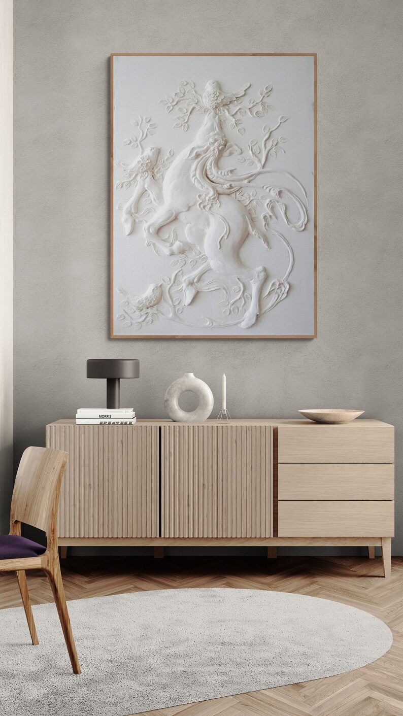 Puede incluir: Una escultura de pared tridimensional blanca de un ciervo con un p&aacute;jaro posado en sus astas. La escultura est&aacute; enmarcada y colgada en una pared gris claro sobre un gabinete de madera.