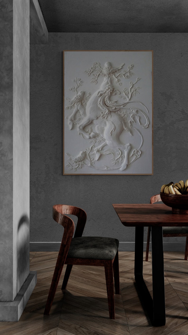Puede incluir: Una escultura en relieve de yeso blanco de una criatura m&iacute;tica con un p&aacute;jaro posado en su cabeza, colocada contra una pared gris en un comedor moderno con una mesa y sillas de madera.
