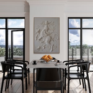 Puede incluir: Un comedor blanco con un gran cuadro blanco enmarcado de una escultura 3D de una mujer montando una criatura m&iacute;tica. El cuadro est&aacute; colgado en una pared blanca sobre una mesa blanca con seis sillas negras. Hay un cuenco de naranjas sobre la mesa.