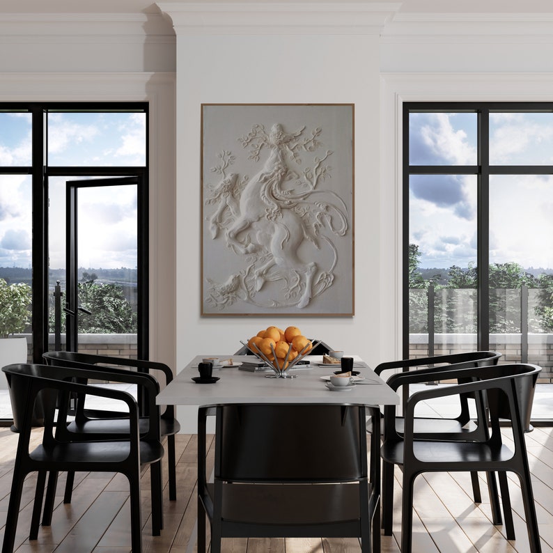Puede incluir: Un comedor blanco con un gran cuadro blanco enmarcado de una escultura 3D de una mujer montando una criatura m&iacute;tica. El cuadro est&aacute; colgado en una pared blanca sobre una mesa blanca con seis sillas negras. Hay un cuenco de naranjas sobre la mesa.