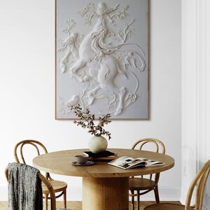 Puede incluir: Una escultura blanca en tres dimensiones de una criatura m&iacute;tica con alas, sobre un fondo blanco, cuelga sobre una mesa de madera con cuatro sillas. La mesa est&aacute; decorada con un jarr&oacute;n de flores, una taza y un platillo, y un libro.