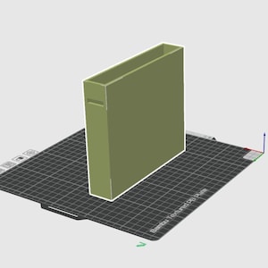 May include: A 3D-rendered olive green rectangular box with a rectangular opening at the top. The box has a small rectangular cutout on one side. The box is on a black grid-like surface.