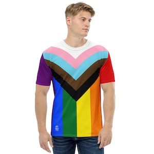 May include: A short-sleeved t-shirt featuring a vibrant, multi-colored design. The shirt's pattern incorporates the colors of the Progress Pride flag, including pink, light blue, brown, black, red, orange, yellow, green, and purple. The shirt has a white neckline.