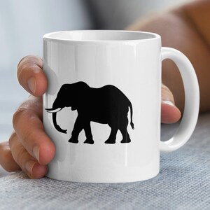 Könnte beinhalten: Weißer Keramikbecher mit einer schwarzen Elefanten-Silhouette. Der Elefant ist im Profil dargestellt, mit Rüssel und Stoßzähnen. Der Becher hat einen gebogenen Henkel und eine glänzende Oberfläche. Geeignet für heiße oder kalte Getränke.