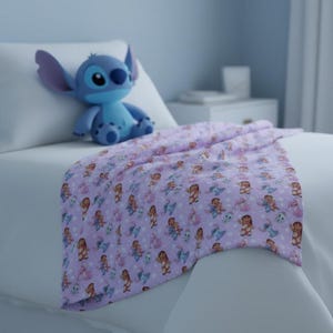 Peut inclure: Une couverture lilas avec un motif r&eacute;p&eacute;t&eacute; de personnages de dessins anim&eacute;s, dont un extraterrestre bleu et une jeune fille. Une peluche bleue du personnage extraterrestre est pos&eacute;e sur un oreiller blanc. La couverture est drap&eacute;e sur un lit.