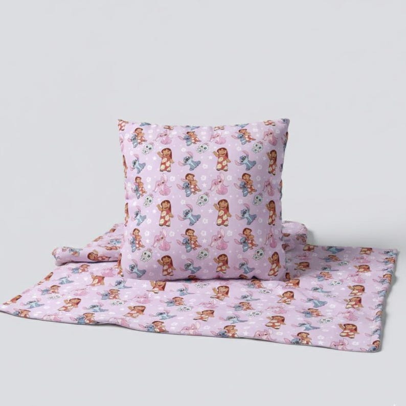 Peut inclure: Un ensemble de coussin et de couverture lavande avec un motif r&eacute;p&eacute;t&eacute; de personnages de dessins anim&eacute;s. Les personnages incluent une fille et un extraterrestre bleu. L'ensemble est con&ccedil;u pour une chambre d'enfant.
