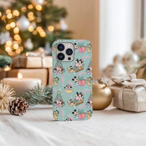May include: A light teal phone case featuring a repeating pattern of Mickey and Minnie Mouse in holiday scenes. The design includes Christmas trees, gift boxes, and the phrase "Merry Christmas" in pink.