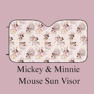 May include: A car sun visor featuring a repeating pattern of Mickey and Minnie Mouse characters, castles, teacups, and Dumbo on a light pink background. The text Mickey & Minnie Mouse Sun Visor is printed below the visor in black serif font.
