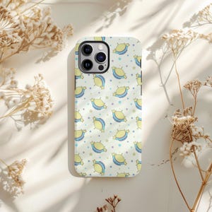 Op de afbeelding: Een telefoonhoesje met een herhaald patroon van gele snoepjes met blauwe en witte accenten, en blauwe en paarse sterren op een lichtcrèmekleurige achtergrond. De hoes heeft een camera-uitsparing en knoppen.
