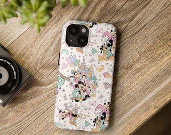 May include: A phone case with a repeating pattern of Disney characters such as Mickey and Minnie Mouse, Donald Duck, and Goofy. The design includes a castle, balloons, and stars on a light background. The case is on a wooden surface.