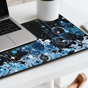May include: A black and blue mouse pad with a design of stars, circles, and swirls. The design is abstract and has a watercolor effect.