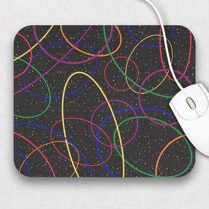 Può includere: Un tappetino per mouse rettangolare con sfondo nero e linee ovali e circolari colorate sovrapposte in giallo, verde, viola e blu. Un mouse per computer bianco con cavo è a destra.