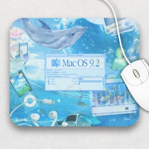 Peut inclure: Une souris d'ordinateur blanche avec un cordon repose sur un tapis de souris avec un motif aquatique bleu. Le tapis de souris présente un dauphin, des notes de musique et le texte "Mac OS 9.2".