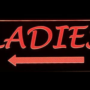 May include: Red neon sign with the word "LADIES" in a cursive font and a red arrow pointing to the left.